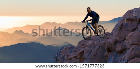 Conquering mountain peaks by cyclist in shorts and jersey on a modern carbon hardtail bike with an air suspension fork . Beautiful view from the mountain. Panoramic view for banner. Royalty-Free Stock Photo #1571777323