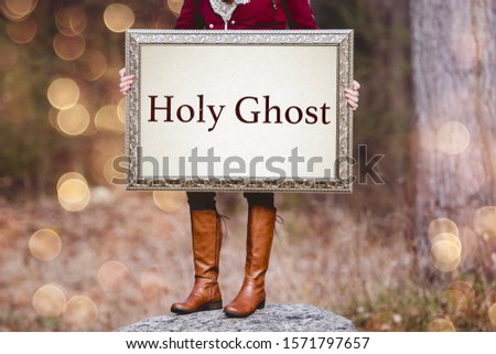 A selective shot of a person holding a picture frame with word "Holy Ghost" written as a text