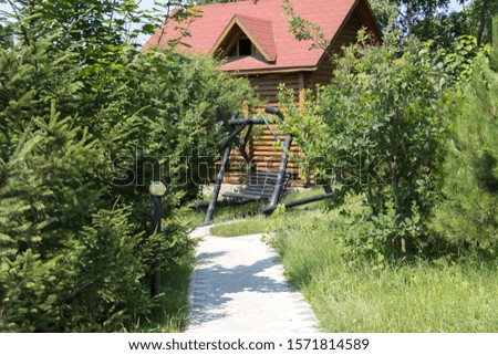 A beautiful horizontal shot of a cabin with a red rooftop and a swing in front, surrounded with trees