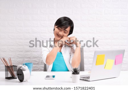Happy woman sitting at home office making a heart gesture with her fingers