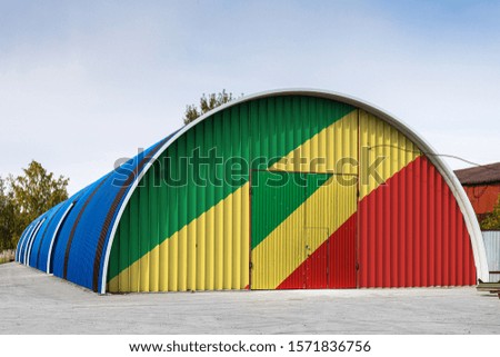 Close-up of the national flag of Republic of the Congo painted on the metal wall of a large warehouse the closed territory against blue sky. The concept of storage of goods, entry to a closed area