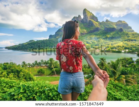 Follow me couple influencers tourists walking on Bora Bora island, Tahiti. Woman leading man off the beaten path exploring nature hiking trail in French Polynesia. Mt Otemanu wanderlust summer travel. Royalty-Free Stock Photo #1571847649