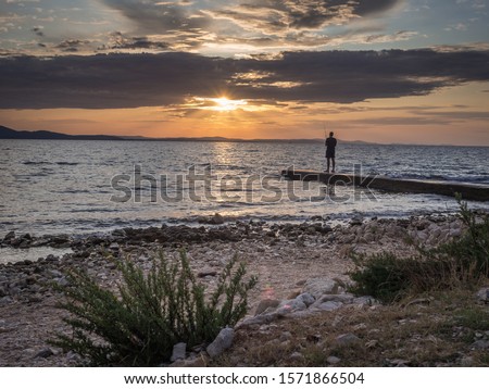 The silhouette of fisherman fishing on the pier in the Zadar city during the colourful sunset. Zadar, Croatia.