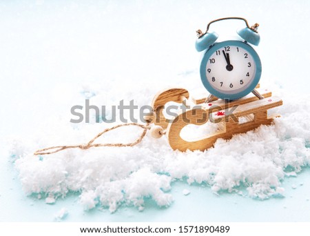 Christmas alarm clock on a wooden sled in the snow shows the time midnight.  Christmas card concept, new year holidays.