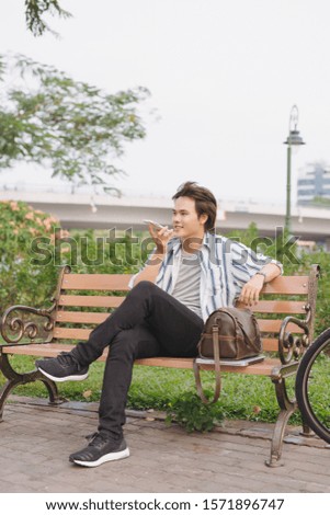 Young man using phone while sitting on bench with bicycle in park
