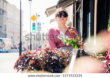 Portrait of Asian woman in stylish clothes standing behind flowers in the street near cafe