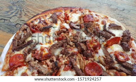 A view of homemade Italian pulled pork pizza on wooden table. It is round, flattened base of leavened wheat-based dough topped with tomatoes, cheese, grilled rump, crisp bacon, pepperoni, pulled pork