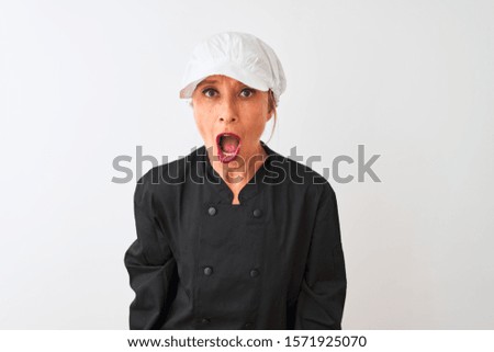 Middle age chef woman wearing uniform and cap standing over isolated white background afraid and shocked with surprise expression, fear and excited face.
