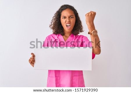 Young brazilian nurse woman holding banner standing over isolated white background annoyed and frustrated shouting with anger, crazy and yelling with raised hand, anger concept