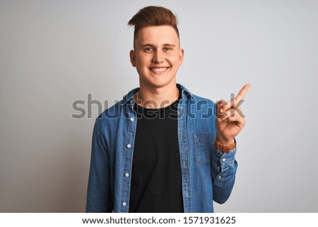 Young handsome man wearing denim shirt standing over isolated white background with a big smile on face, pointing with hand and finger to the side looking at the camera.