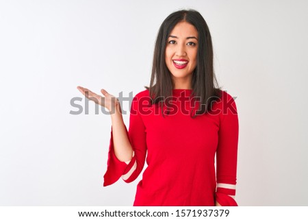 Young beautiful chinese woman wearing red dress standing over isolated white background smiling cheerful presenting and pointing with palm of hand looking at the camera.