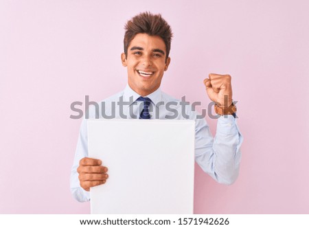 Young handsome businessman holding banner standing over isolated pink background screaming proud and celebrating victory and success very excited, cheering emotion