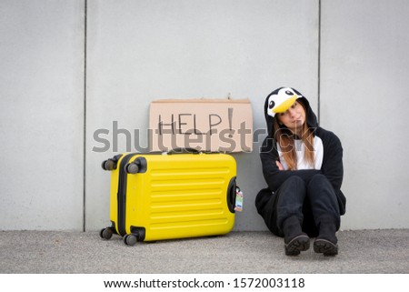 Young woman, with penguin costume and yellow suitcase, has to travel due to global warming. Symbolizes a sad penguin who has to leave his homeland because of global warming or climate change.