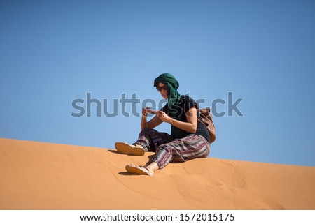 Girl looking at the mobile phone in the dunes of the Moroccan Sahara desert.
