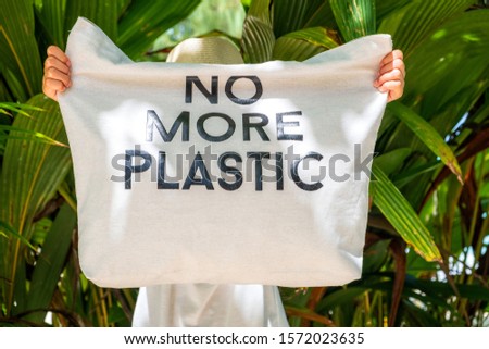 Young girl holding eco bag with sign No More Plastic on tropical beach background  Royalty-Free Stock Photo #1572023635