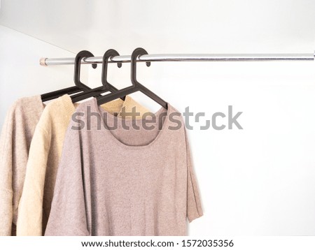 Knitted Sweaters and cardigans in beige grey neutral tone hanging  in wardrobe. Fall winter season cloth concept.