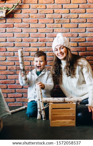 Mom with son in knitted sweaters playing, stacking firewood in a drawer. Winter New Year and Christmas mood