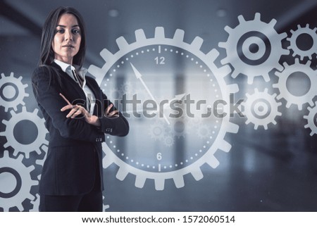 Attractive businesswoman and glowing cogwheel hologram interface on blurry office interior background. Teamwork and mechanism concept.