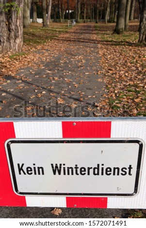 A red and white sign on a footpath at the entrance of a park in Nuremberg informs Kein Winterdienst  (in English: no winter service ). Seen in Franconia / Bavaria in Germany in November.