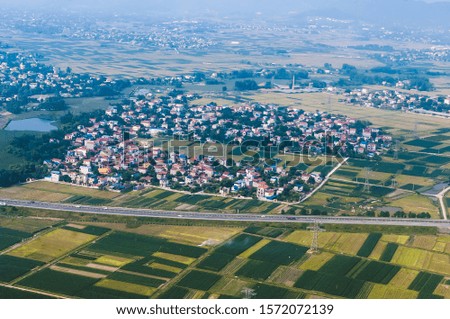Aerial shot, landscape photography, view from above of a highway going through farmland fields and a small town of the countryside, on the outskirts of Hanoi, Vietnam in hot sunset evening. 
