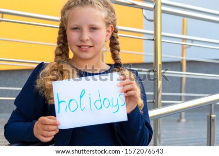happy girl holding  paper with the words holidays. Concept School holidays,graduation.  girl in a  uniform. pupil, learner, scholar. happy schoolgirl