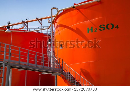 Oil refinery plant warehouse. Orange metal storage tanks with sulfuric acid and its formula on tank. Close-up photo. Royalty-Free Stock Photo #1572090730