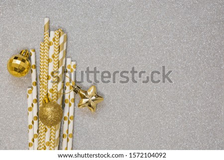 Christmas golden balls and drinking golden straw on silver background. Trendy color Ultimate Grey of the 2021 year. Flat lay, top view, copy space. Holiday Greeting card. Cocktail party invitation.