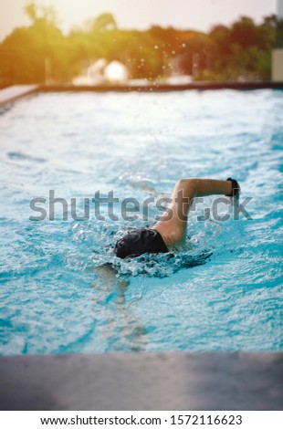 Young fit girl in goggles and cap swimming freestyle stroke in the blue water pool with light, exercise and training lifestyle