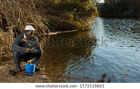 Portrait of bored African man fishing with rods on river