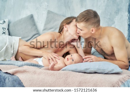 young nursing mother kisses her husband and play with newborn baby