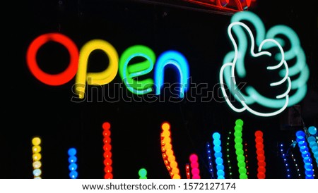 A glowing neon Open sign with a thumbs up character on a black background