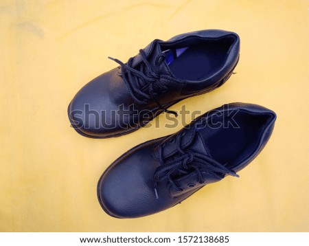 Black Color School Shoes for Little Boy.  Black Shoes Isolated on Yellow Non Woven Fabric Background. Classic Shoes with Laces.
