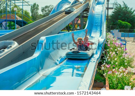 Children on a water slide, two boys descend on an inflatable boat in an amusement park.