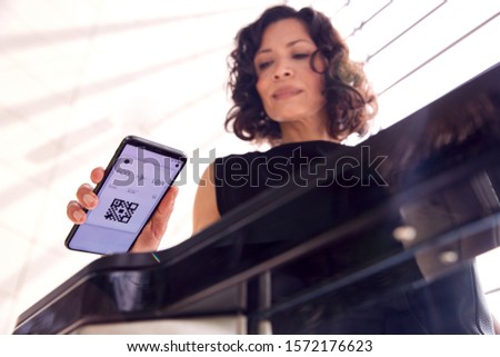 Businesswoman In Airport Departure Lounge Scanning Digital Boarding Pass On Smart Phone Royalty-Free Stock Photo #1572176623