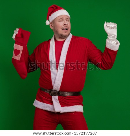 Santa Claus holds a Christmas sock for gifts in his hands and poses on a green chrome background