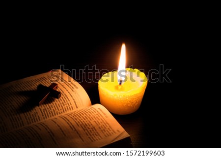 Burning candle and Bible . The psalms . Holy book  .  told in the Bible's New Testament , on a black background . Christian cross .