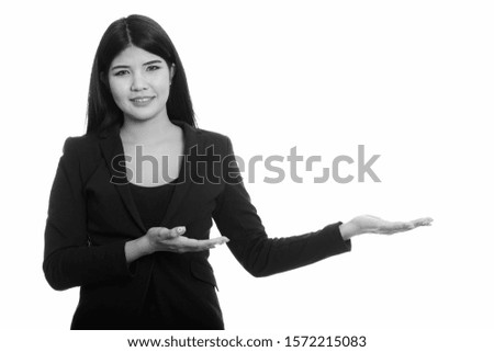 Studio shot of young happy Asian businesswoman smiling and showing something