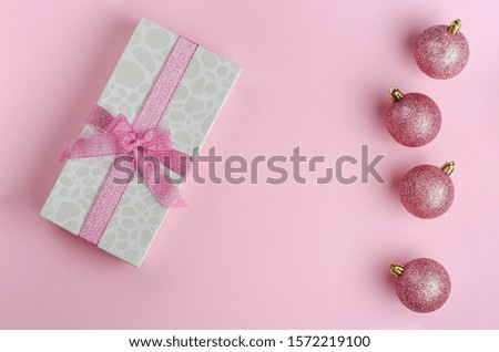 Christmas minimalistic composition. Gift box with ribbon and baubles on pink background. Flat lay, copy space. Greeting card concept.