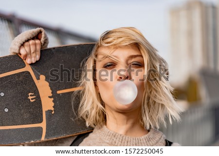 Urban stylish young girl walking with skateboard. Outdoors portrait of active sport woman model. Healthy lifestyle. Extreme sports. Close up portrait of a pretty young girl chewing bubble gum.