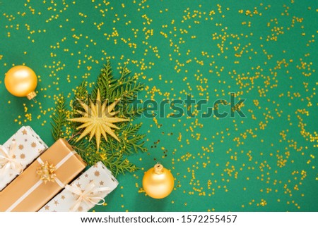 Festive background with decorations , bright gold star and gift boxes and christmas balls on a green background with glitter gold stars, flat lay, top view, copy space
