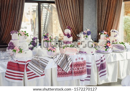 Wedding breads and cakes stand on long table covered with embroidered towels