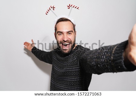 Image of brunette young man in Christmas candy cane headband taking selfie photo isolated over gray background