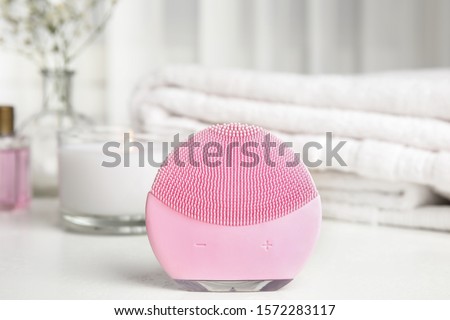 Modern face cleansing brush on white table. Cosmetic accessory
