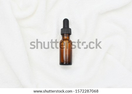 Dark amber dropper bottle mock up on white soft towel, essential oil, serum, elixir, cosmetic oil. 