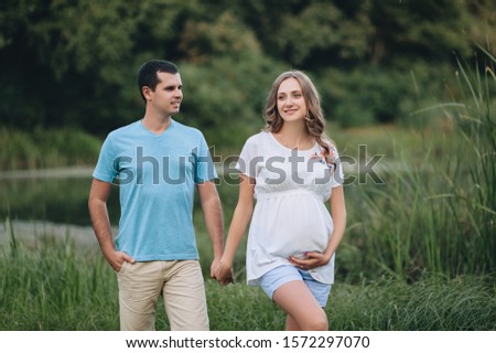 Portrait of a young and smiling family expecting a baby. A loving man and a beautiful pregnant blond woman are walking in the park holding hands. Pregnancy picture, concept.