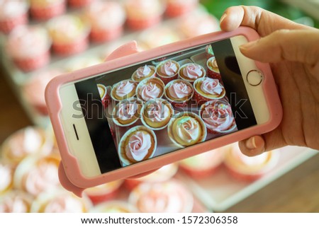 The cafe owner uses a smartphone to take pictures of newly finished cupcakes to promote on online media and websites. Selling products online