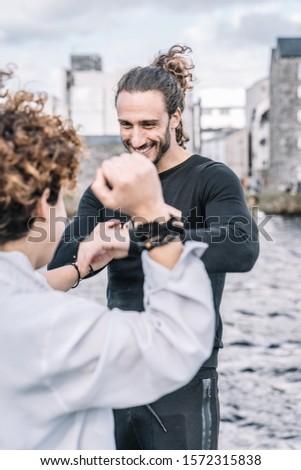 Stock vertical photo of a young couple arguing and fighting with funny expression with buildings and blurred sea background. Lifestyle