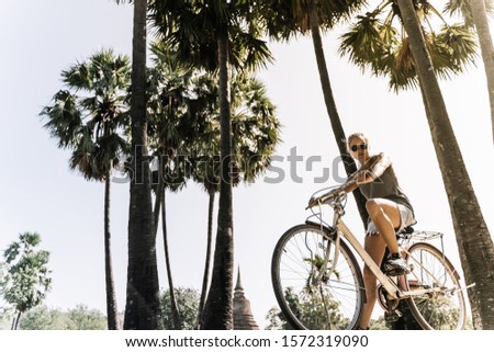 girl on bicycle on a summer day, in a tropical site with palm trees and sun rays in the background. Vintage style stock photo