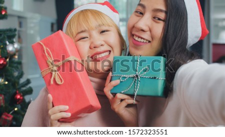 Asian Lesbian couple celebrate Christmas festival. LGBTQ female teen relax happy holding Gift and using smartphone selfie with Christmas tree enjoy xmas winter holidays in living room at home.