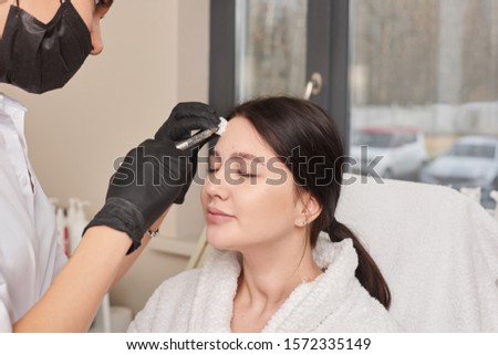 Woman gets beauty facial injections. Anti-aging, nourishing, vitamins treatment at spa salon. Aesthetic cosmetology. Doctor's hand in black surgical glove marking women's face for cosmetic injections.